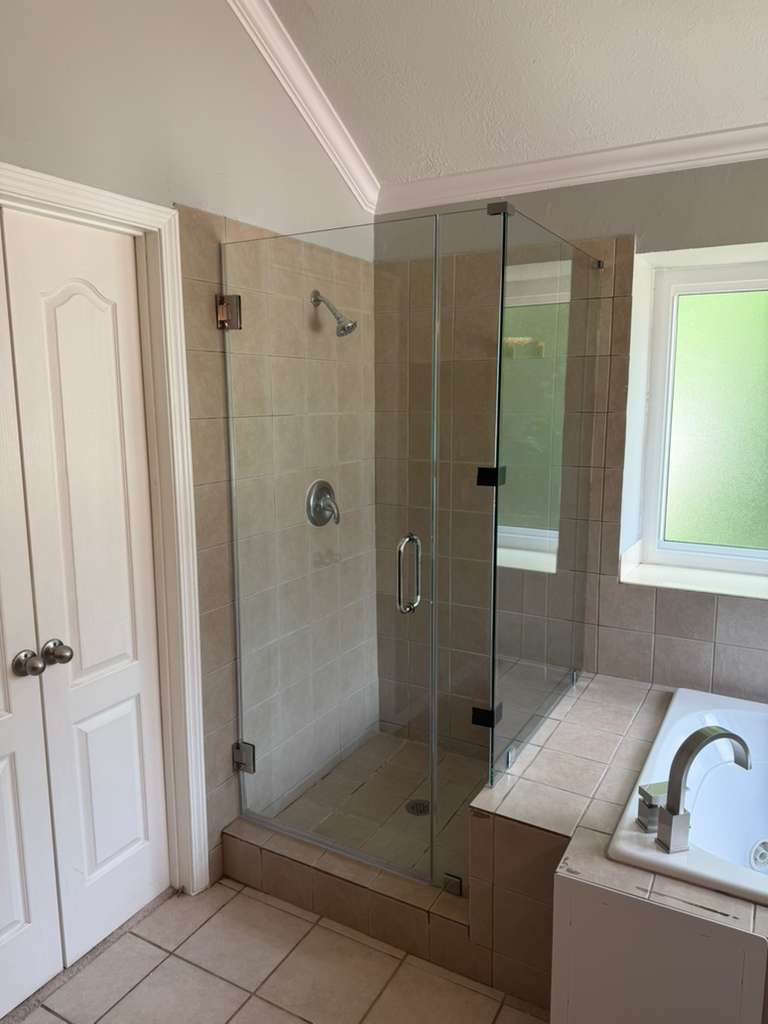 Frameless shower enclosure with tan tile next to jetted tub