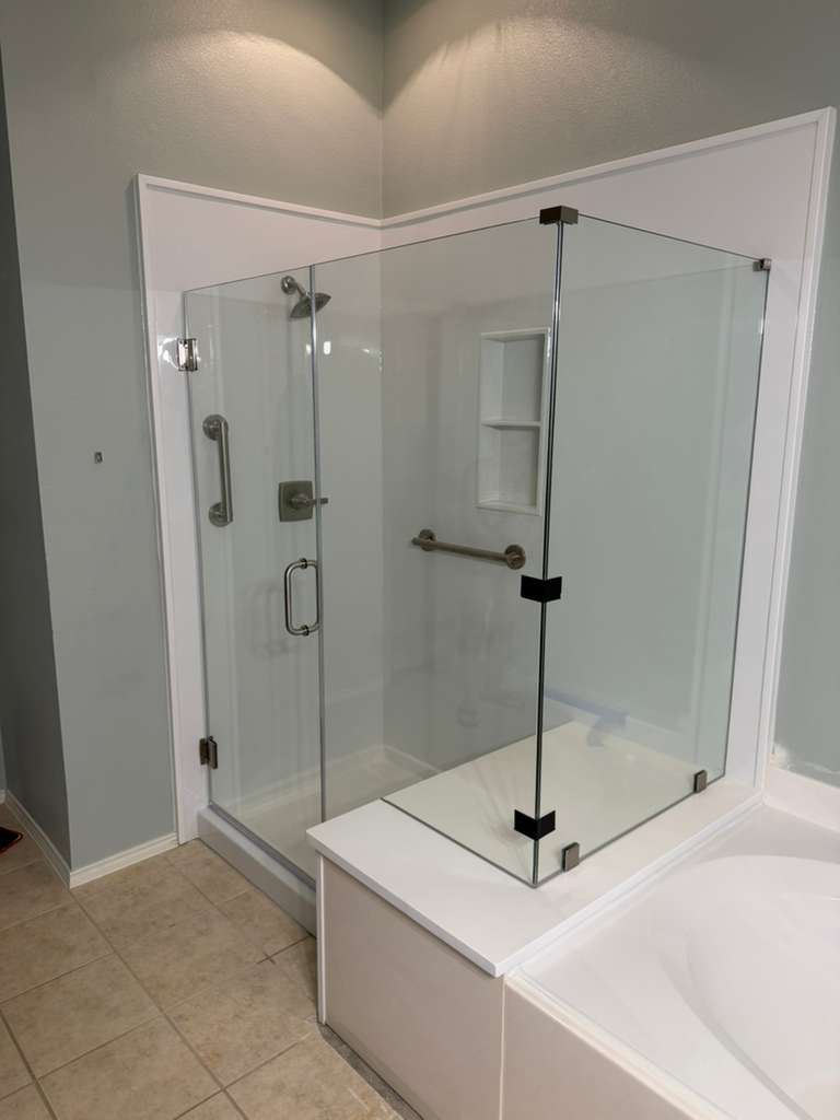 Frameless corner shower with brushed nickel hardware next to soaking tub