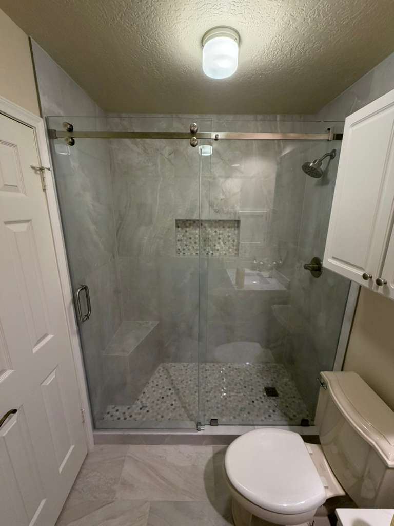 Sliding frameless shower with brushed nickel track and pebble mosaic floor