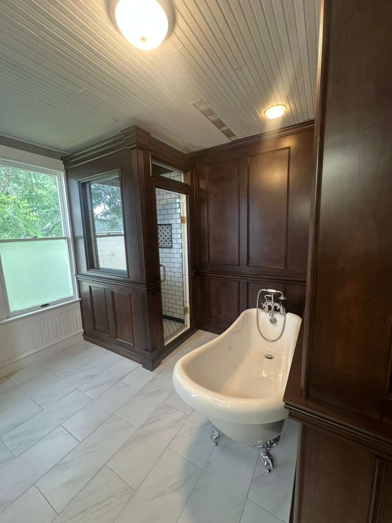 Custom framed shower enclosure in wood-paneled bathroom with clawfoot tub